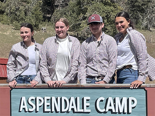 Four FFA students behind ASPENDALE CAMP sign 