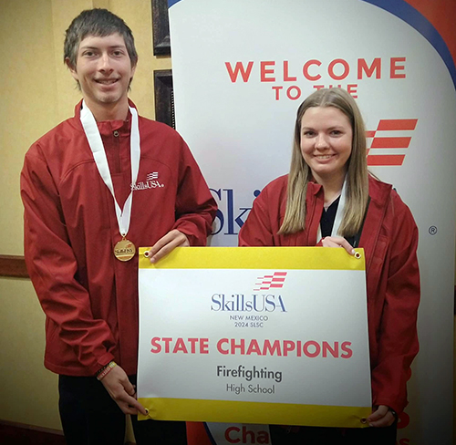 Two students in red jackets holding state champions poster